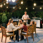 Man bringing BBQ plate to family at an outside patio table